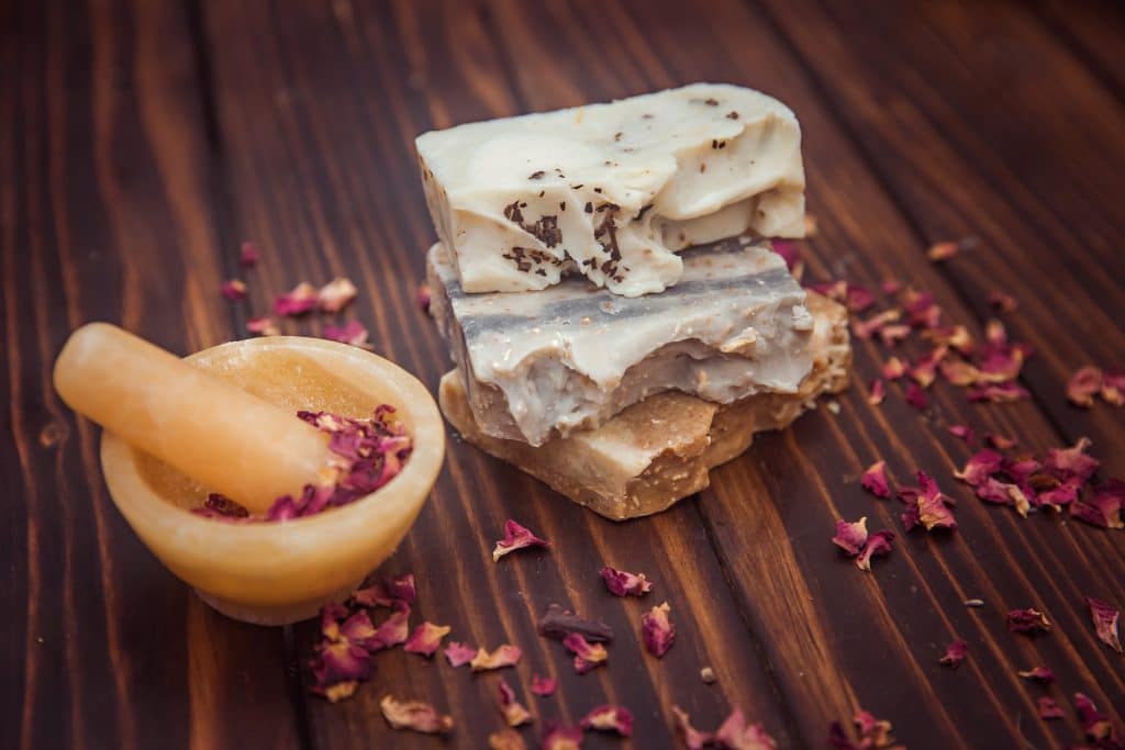 3 bars of soap, a spice grinder, and a sprinkle of dried flowers on a dark wood floor.